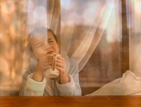 A child with a mug in his hands at the window dreams of looking into the distance.の写真素材