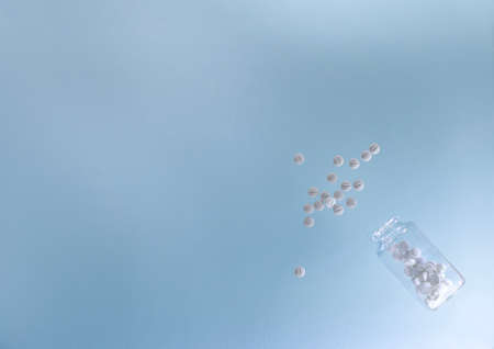 Tablets are white, poured from a transparent jar on a blue surface.の写真素材