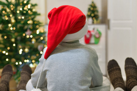 Family at Christmas at the decorated Christmas tree. A child in Santas hat between his parents in socks with ornaments.の写真素材
