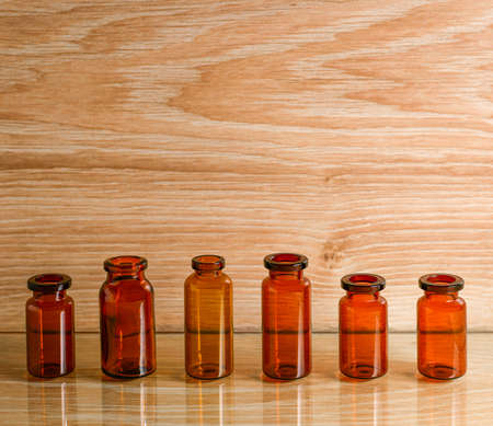 Small empty glass pharmacy bottles in a row on a wooden background.の写真素材