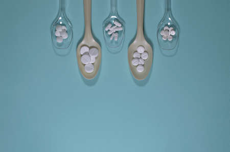 Spoons filled with various pills, on a blue background.の写真素材