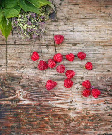 Raspberries on a wooden surface with a bouquet of raspberry leaves and thyme.の写真素材