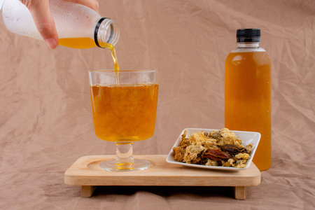 A person pours a liquid into a glass from a bottle on a wooden tray.