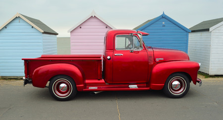 Classic Red  Chevrolet 3100 pickup truck on seafront promenade in front of beach huts.のeditorial素材