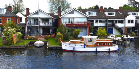 HORNING, NORFOLK, ENGLAND - MAY 10, 2018: Waterside properties and old fashioned cruiser on the river Bure at Horning.のeditorial素材
