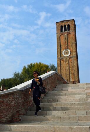 MURANO, VENICE, ITALY - SEPTEMBER 23, 2017: Female Tourist on Bridge on the Island of Murano Venice, bell tower in background.のeditorial素材