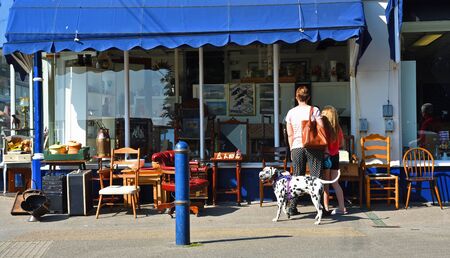 FELIXSTOWE, SUFFOLK, ENGLAND - APRIL 21, 2019: Antique Shop with furniture on pavement outside and customers looking in window with Dalmatian Dog .のeditorial素材