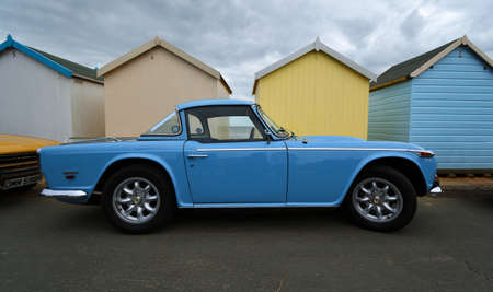 FELIXSTOWE, SUFFOLK, ENGLAND - MAY 05, 2019: Classic Light Blue Triumph TR5 2500 PI  Motor Car parked on seafront promenade with beach Huts  in background.のeditorial素材