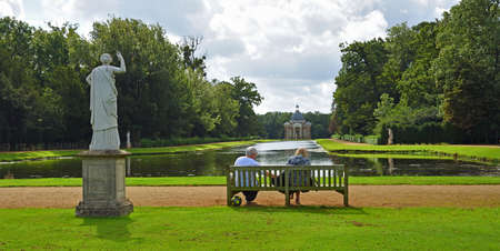 SILSOE, BEDFORDSHIRE, ENGLAND -  SEPTEMBER 04, 2020: Couple sitting on bench overlooking the Thomas Archer pavillion and Long Canal at Wreat Park.のeditorial素材