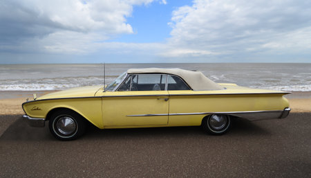 Classic  yellow Ford Sunliner Convertible Car parked on seafront promenade sea and beach in background.のeditorial素材