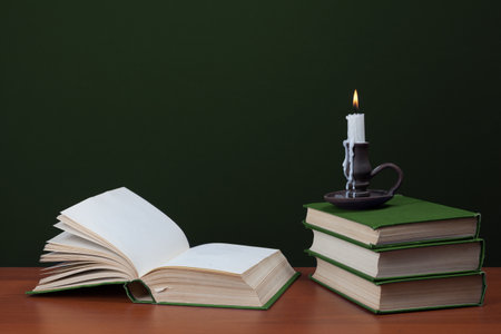 open blank book and stack of books with burning candles on green backgroundの写真素材