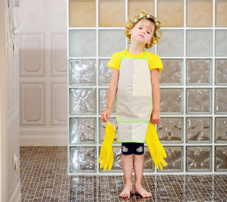 A little girl in curlers, apron and gloves is cleaning in the bathroom.の写真素材