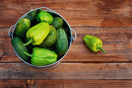 A full bucket of green peppers and cucumbers stands on a wooden benchの写真素材