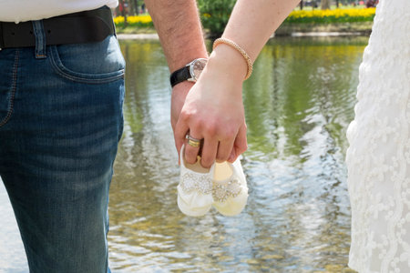 Future mother and father is waiting their baby. They are holding baby shoes and hands. there are red...