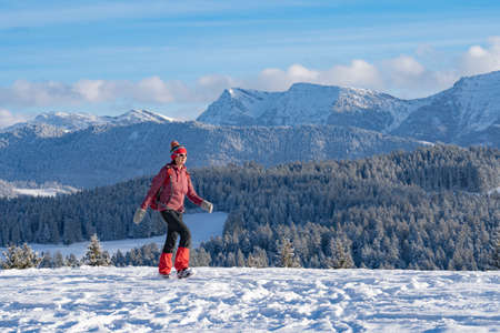 nice active senior woman snowshoeing in the Allgaeu Alps near Oberstaufen with view into the Bregenzerwald, Vorarlberg, Austriaの写真素材
