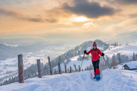 nice active senior woman snowshoeing in the Allgaeu Alps near Oberstaufen with view into the Bregenzerwald, Vorarlberg, Austriaの写真素材