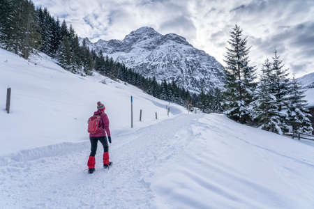 active senior woman hiking in the snowy mountains of Kleinwalsertal, Vorarlberg, Austria, near village of Baad, below the summit of Widdersteinの写真素材