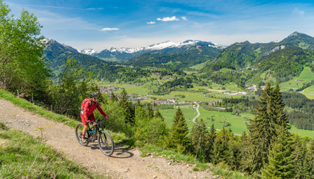 pretty senior woman riding her electric mountain bike on the Wallraff Trail in the Nebelhorn area above Oberstdorf, Allgau Alps, Bavaria,の写真素材