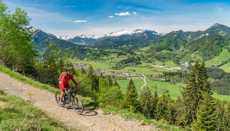 pretty senior woman riding her electric mountain bike on the Wallraff Trail in the Nebelhorn area above Oberstdorf, Allgau Alps, Bavaria,の写真素材