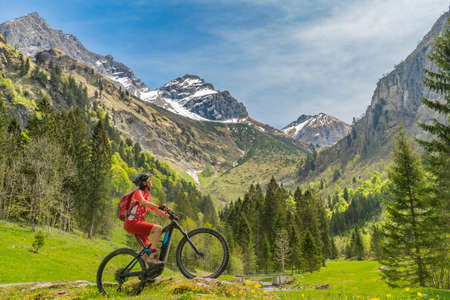 pretty senior woman riding her electric mountain bike the Oy Tal Valley near Oberstdorf, Allgau Alps, Bavaria, Germanyの写真素材