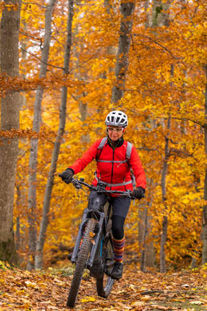 sympathetic active senior woman, riding her electric mountain bike in the gold colored autumn forests of the Swabian Albの写真素材