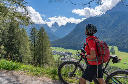 nice and active senior woman riding her electric mountain bike on a old military road from Toblach upt to the summit of Marchkinkele eith spectacular view to the Three peaks of Lavaredo, South Tirol,の写真素材