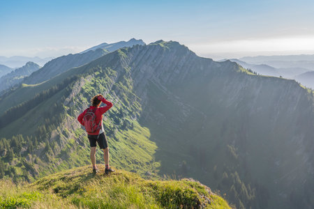 pretty senior woman resting during a hike in the early evening in warm dawn light on the ridge of the Nagelfluh chain in the Allgau Alps near Immenstadt, Bavaria, Germanyの写真素材