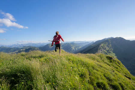 active senior woman mountain running in the early evening in warm dawn light on the ridge of the Nagelfluh chain in the Allgau Alps near Immenstadt, Bavaria, Germanyの写真素材