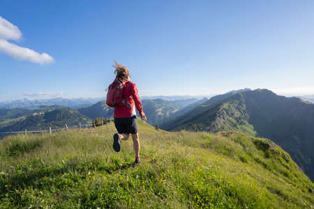 active senior woman mountain running in the early evening in warm dawn light on the ridge of the Nagelfluh chain in the Allgau Alps near Immenstadt, Bavaria, Germanyの写真素材
