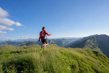 active senior woman mountain running in the early evening in warm dawn light on the ridge of the Nagelfluh chain in the Allgau Alps near Immenstadt, Bavaria, Germanyの写真素材