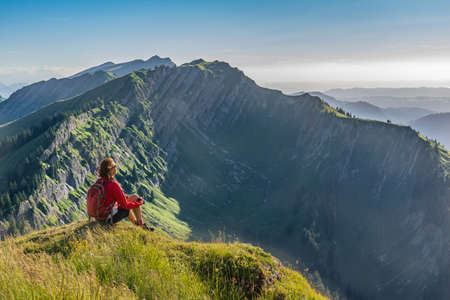 pretty senior woman resting during a hike in the early evening in warm dawn light on the ridge of the Nagelfluh chain in the Allgau Alps near Immenstadt, Bavaria, Germanyの写真素材