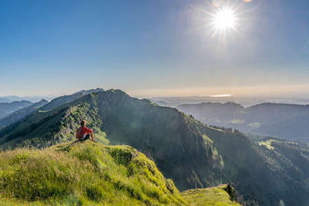 pretty senior woman resting during a hike in the early evening in warm dawn light on the ridge of the Nagelfluh chain in the Allgau Alps near Immenstadt, Bavaria, Germanyの写真素材