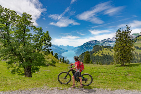 active woman riding her electric mountain bike below the seven summits of Churfirsten, enjoying the awesome view down to Lake Walensee Canton St. Gallen, Switzerlandの写真素材