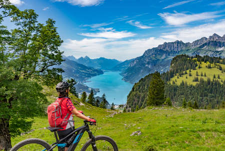 active woman riding her electric mountain bike below the seven summits of Churfirsten, enjoying the awesome view down to Lake Walensee Canton St. Gallen, Switzerlandの写真素材