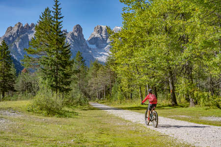 nice and active senior woman riding her electric mountain bike on an old railway embankment in the Hoehlenstein valley between Toblach and Cortina Dampezzo, Three Peaks Dolomites, South Tirol, Italyの写真素材