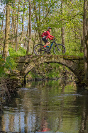 nice active senior woman riding her electric mountain bike in early spring along the little river Glems near Stuttgart, Baden-Wuerttemberg, Germanyの写真素材