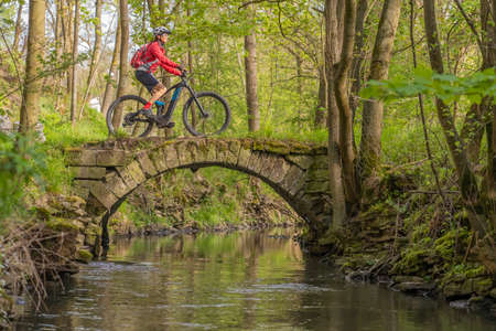 nice active senior woman riding her electric mountain bike in early spring along the little river Glems near Stuttgart, Baden-Wuerttemberg, Germanyの写真素材