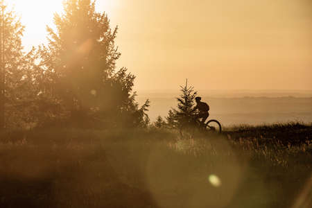 pretty senior woman riding her electric mountain bike in warm dawn sunlight below the summit cross of Salmas hight above Oberstaufen, Allgau Alps, Bavaria Germanyの写真素材