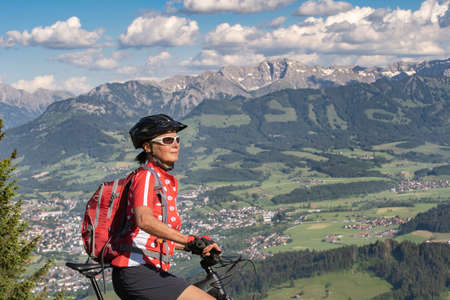 pretty senior woman riding her electric mountain bike on the mountains above the Iller valley between Sonthofen and Oberstdorf, Allgau Alps, Bavaria Germanyの写真素材