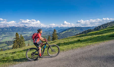 pretty senior woman riding her electric mountain bike on the mountains above the Iller valley between Sonthofen and Oberstdorf, Allgau Alps, Bavaria Germanyの写真素材