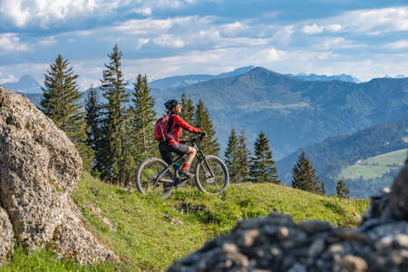pretty senior woman riding her electric mountain bike in warm dawn sunlight and enjoying the spectacular view over the Allgau alps near Oberstdorf, Bavaria, Germanyの写真素材