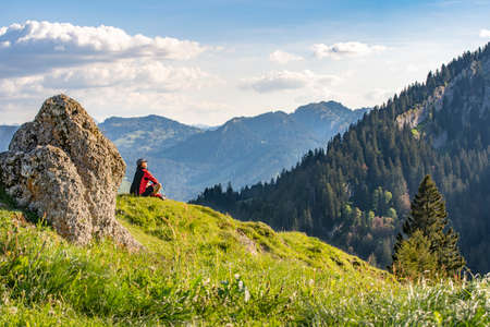 pretty senior woman hiking in warm dawn sunlight and enjoying the spectacular view over the Allgau alps near Oberstdorf, Bavaria, Germanyの写真素材