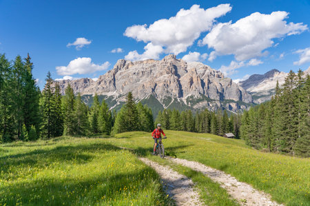 beautiful active senior woman riding her electric mountain bike on the Pralongia Plateau in the Alta Badia Dolomites with awesome Sasso die Santa Cruce summit in Backg, South Tirol and Trentino, Italyの写真素材