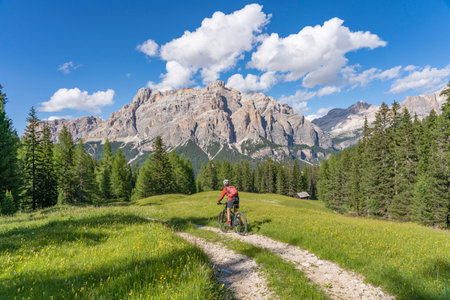 beautiful active senior woman riding her electric mountain bike on the Pralongia Plateau in the Alta Badia Dolomites with awesome Sasso die Santa Cruce summit in Backg, South Tirol and Trentino, Italyの写真素材