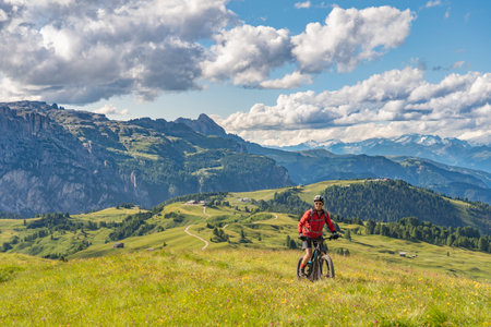 beautiful active senior woman riding her electric mountain bike on the Pralongia Plateau in the Alta Badia Dolomites with awesome Sasso die Santa Cruce summit in Backg, South Tirol and Trentino, Italyの写真素材