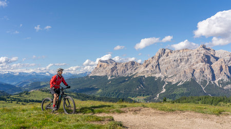 beautiful active senior woman riding her electric mountain bike on the Pralongia Plateau in the Alta Badia Dolomites with awesome Sasso die Santa Cruce summit in Backg, South Tirol and Trentino, Italyの写真素材