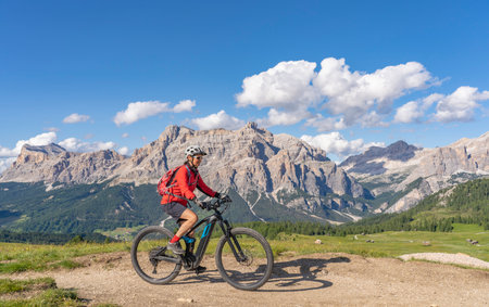 beautiful senior woman riding her electric mountain bike on the Pralongia Plateau in the Alta Badia Dolomites with awesome Sasso die Santa Cruce summit in Backg, South Tirol and Trentino, Italyの写真素材