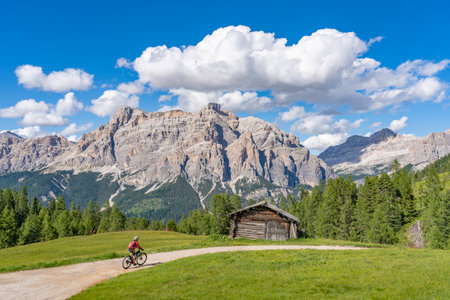 beautiful active senior woman riding her electric mountain bike on the Pralongia Plateau in the Alta Badia Dolomites with awesome Sasso die Santa Cruce summit in Backg, South Tirol and Trentino, Italyの写真素材