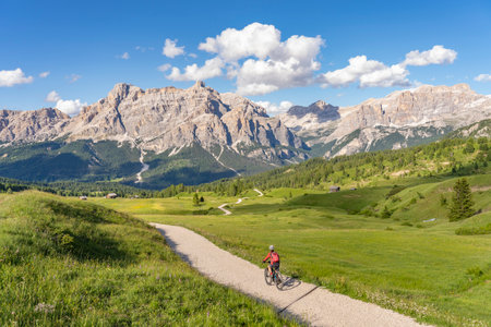beautiful active senior woman riding her electric mountain bike on the Pralongia Plateau in the Alta Badia Dolomites with awesome Sasso die Santa Cruce summit in Backg, South Tirol and Trentino, Italyの写真素材