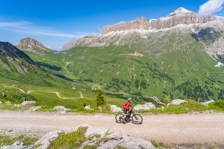beautiful aczive senior woman riding the famous Sella Ronda mountain bike Trail in Sella mountain group, Dolomites of Selva Wolkenstein, Val Gardena, South Tirol and Trentino, Italyの写真素材
